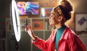 Influencer standing in front of a phone with a ring light. 